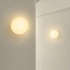 Arendal opal glass wall lights lit on a plaster wall at two sizes