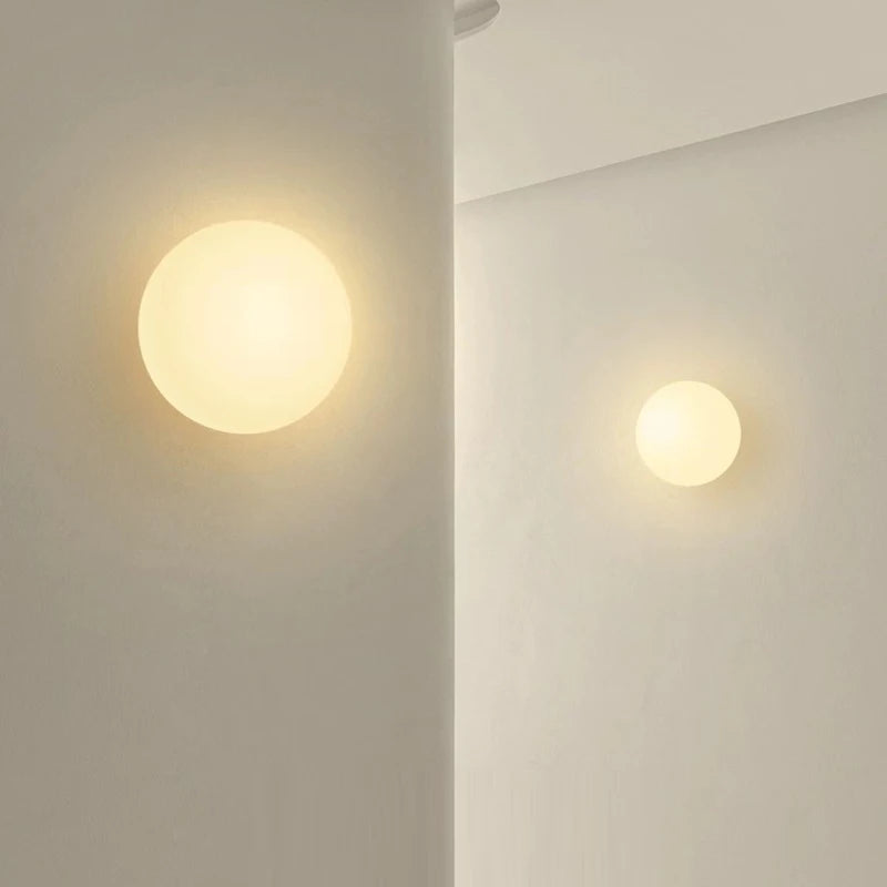 Kettlewell opal glass wall lights lit on a plaster wall at two sizes