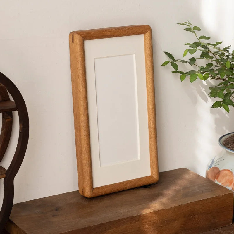Gorlitz teak tone frame on a wooden shelf beside a plant