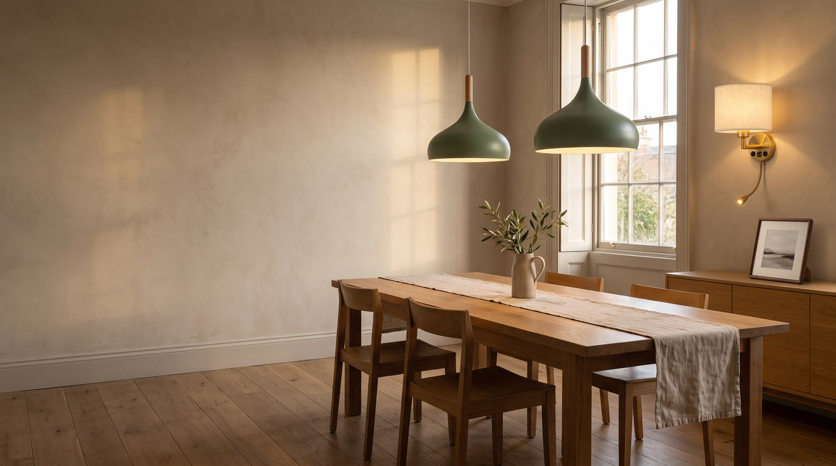 Two sage green Kalix dome pendants over an oak dining table, with a brass Middelfart wall light and a walnut Stralsund frame in a warm townhouse dining room