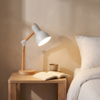 Elmsworth desk lamp lit on an oak bedside table beside linen bedding