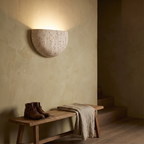 Inglecote travertine wall light above an oak bench in a plastered hallway