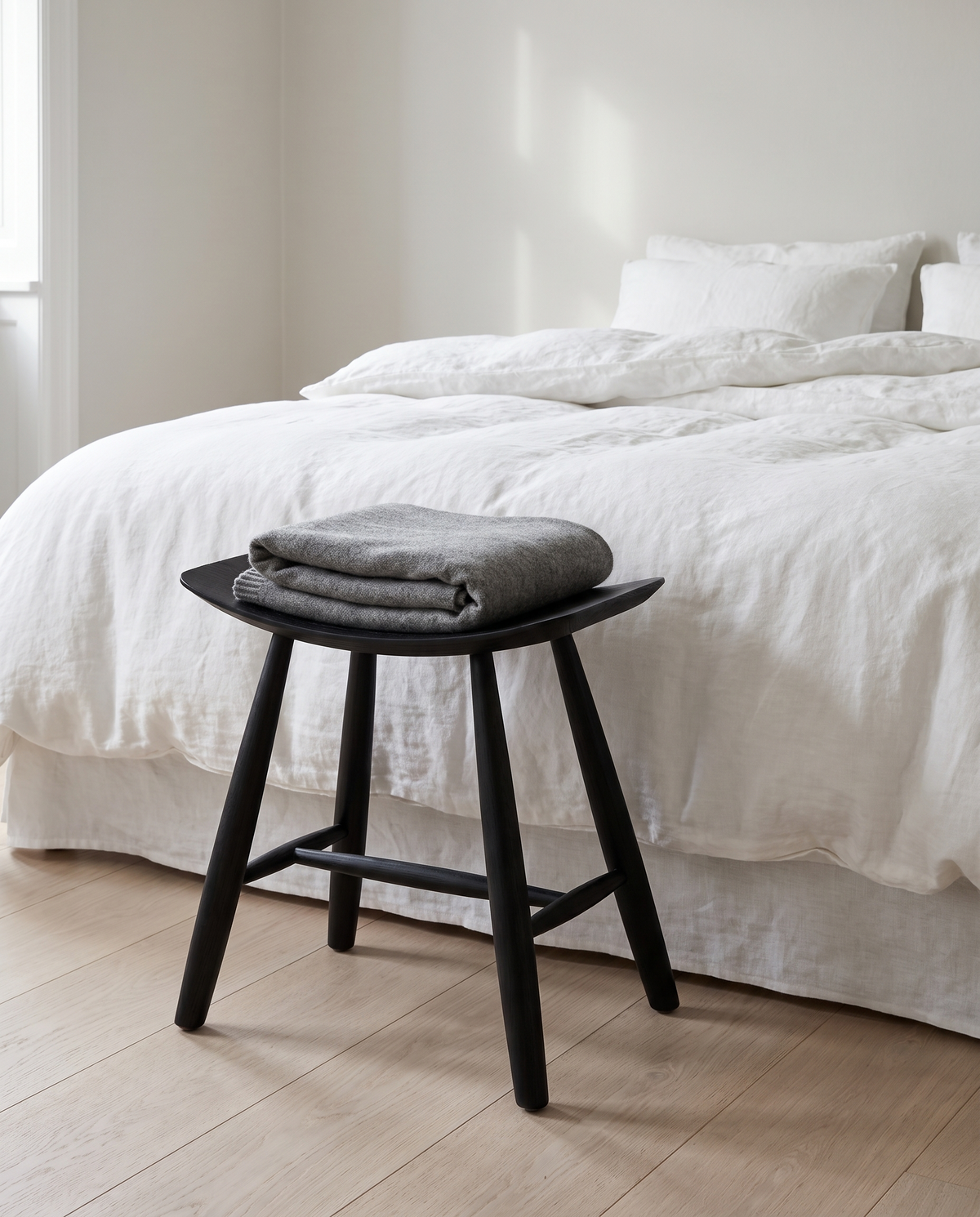 Herning saddle stool in black at the foot of a bed
