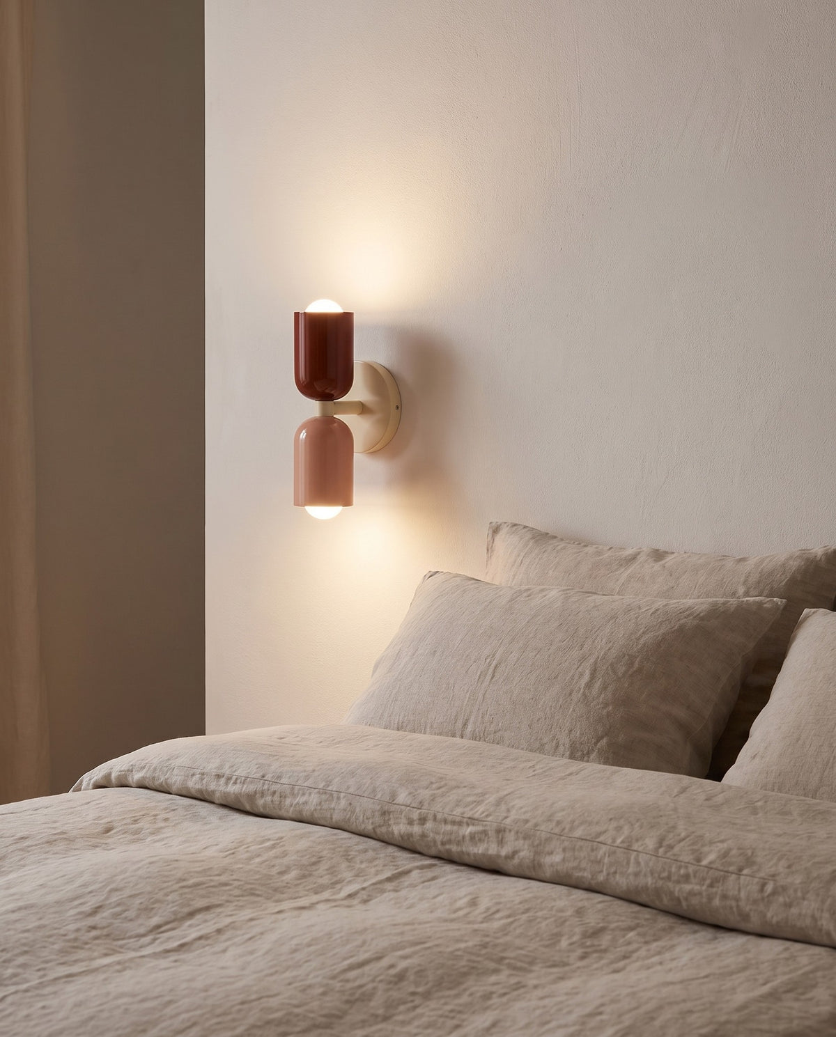 Thun rust and blush wall light glowing beside a bed